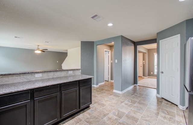 kitchen featuring light stone countertops, dark brown cabinets, stainless steel refrigerator, ceiling fan, and light tile floors