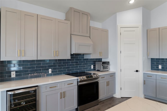 kitchen with stainless steel electric range, beverage cooler, exhaust hood, gray cabinets, and decorative backsplash