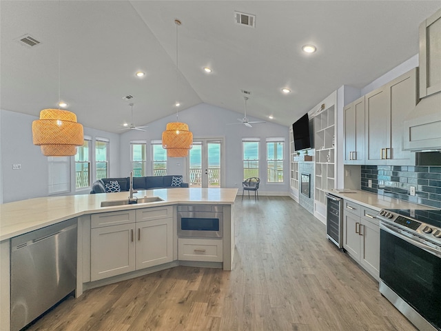 kitchen with sink, vaulted ceiling, beverage cooler, stainless steel appliances, and light hardwood / wood-style floors