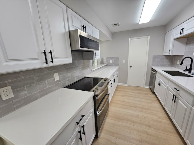 kitchen with white cabinetry, sink, tasteful backsplash, appliances with stainless steel finishes, and light wood-type flooring