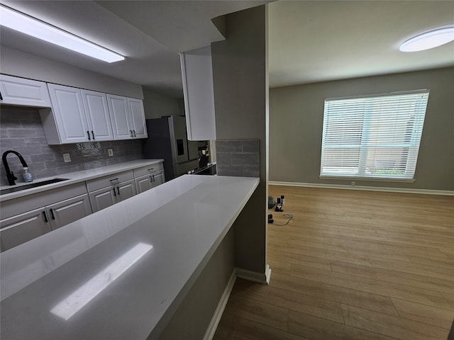 kitchen featuring white cabinetry, sink, light hardwood / wood-style flooring, backsplash, and stainless steel fridge