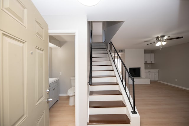 staircase featuring ceiling fan, wood-type flooring, and a fireplace