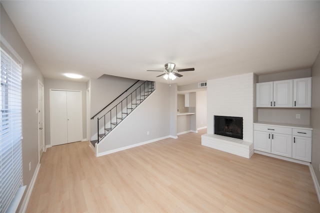 unfurnished living room with light wood-type flooring, a brick fireplace, and ceiling fan