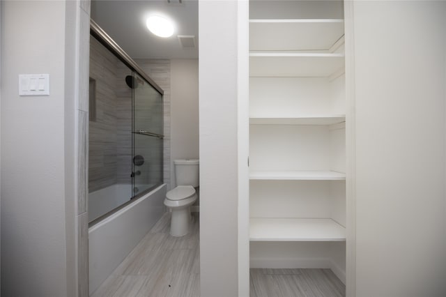 bathroom featuring toilet and bath / shower combo with glass door