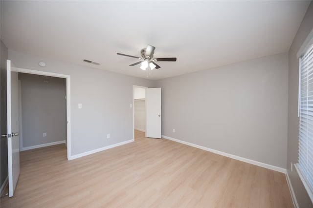 unfurnished bedroom with a walk in closet, a closet, light hardwood / wood-style flooring, and ceiling fan