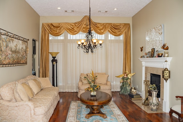 living room featuring a textured ceiling, dark hardwood / wood-style flooring, a tile fireplace, and an inviting chandelier