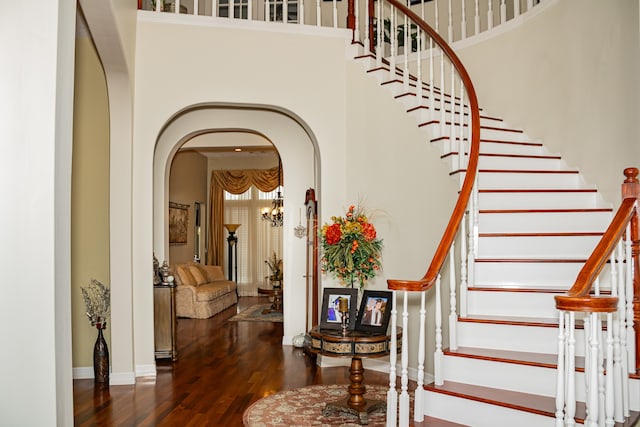 staircase with hardwood / wood-style floors, a towering ceiling, and an inviting chandelier