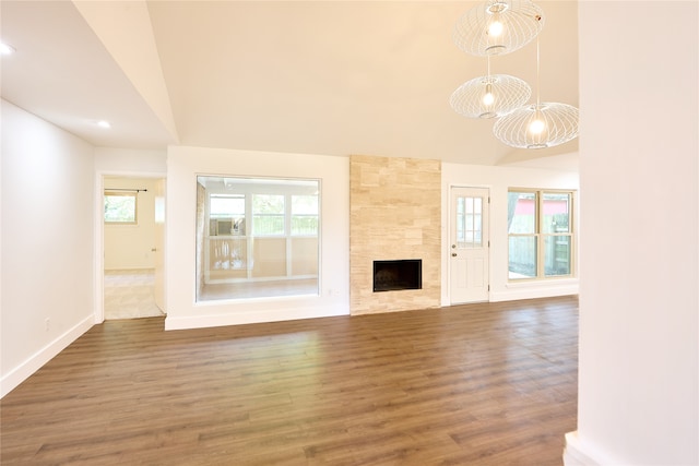 unfurnished living room with dark wood-type flooring, a tiled fireplace, an inviting chandelier, and vaulted ceiling