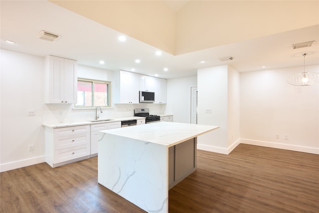 kitchen with dark wood-type flooring, light stone counters, a center island, white cabinetry, and appliances with stainless steel finishes