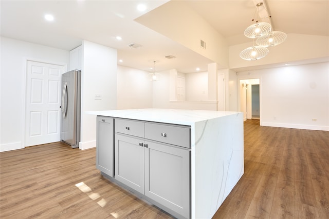 kitchen with light stone countertops, decorative light fixtures, light hardwood / wood-style floors, and a center island