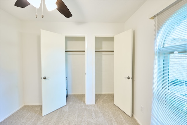 unfurnished bedroom featuring two closets, light carpet, and ceiling fan