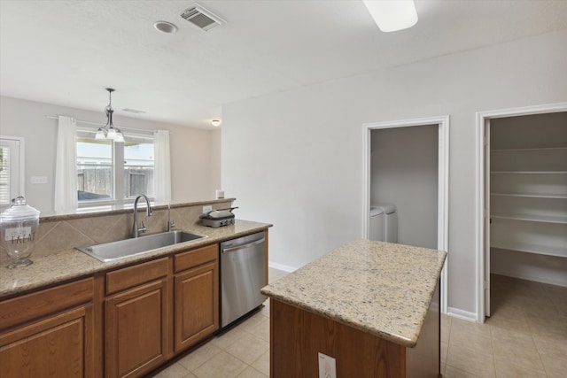 kitchen with washer and dryer, light tile floors, a kitchen island, sink, and stainless steel dishwasher