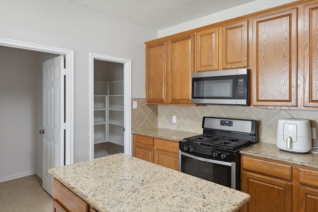 kitchen featuring backsplash, gas stove, light tile floors, and light stone counters