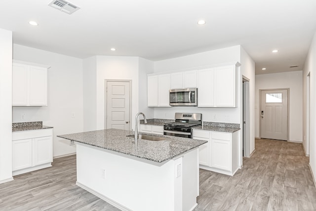 kitchen with appliances with stainless steel finishes, light hardwood / wood-style flooring, sink, and an island with sink