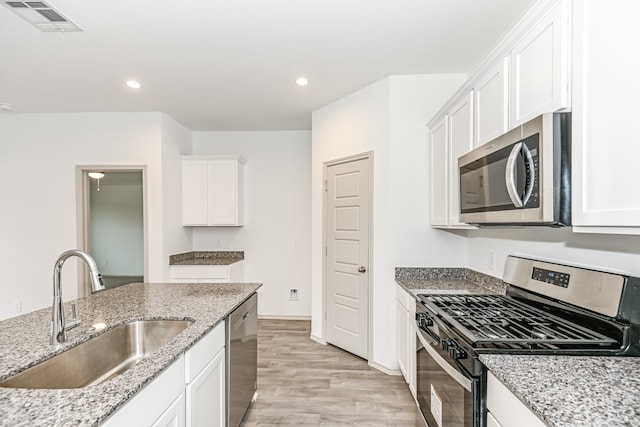 kitchen with white cabinetry, stainless steel appliances, light hardwood / wood-style floors, light stone counters, and sink