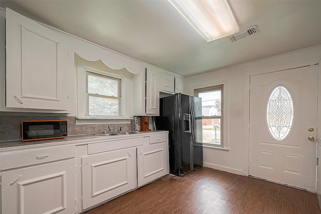 kitchen featuring white cabinets, black fridge, a wealth of natural light, and dark wood-type flooring