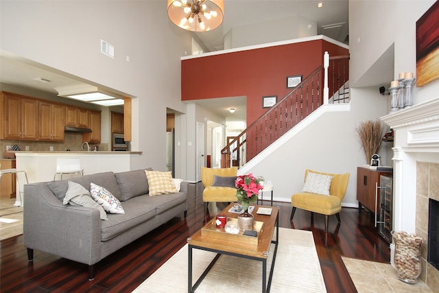 living room with an inviting chandelier, a towering ceiling, hardwood / wood-style flooring, and a tiled fireplace