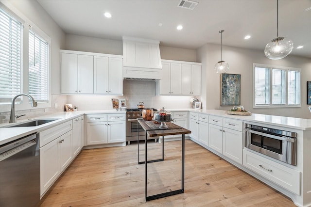 kitchen featuring white cabinets, hanging light fixtures, stainless steel appliances, light countertops, and a sink