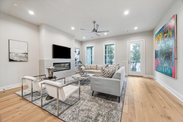 living room with a glass covered fireplace, baseboards, light wood finished floors, and recessed lighting