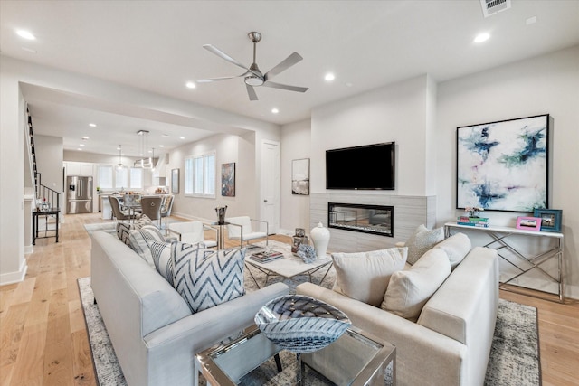 living room featuring recessed lighting, visible vents, light wood-style flooring, a glass covered fireplace, and ceiling fan