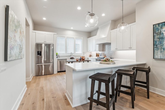 kitchen with white cabinets, hanging light fixtures, stainless steel appliances, light countertops, and premium range hood