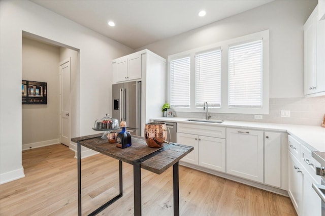 kitchen featuring white cabinets, appliances with stainless steel finishes, light countertops, light wood-style floors, and a sink