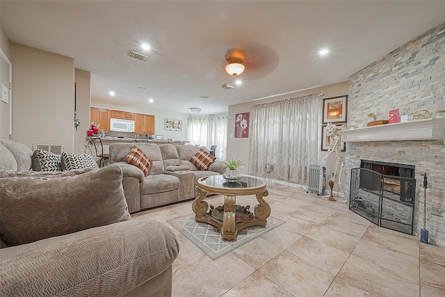 living room with ceiling fan, a stone fireplace, and light tile floors