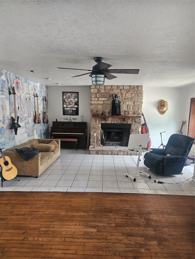 tiled living room with ceiling fan, a stone fireplace, and a textured ceiling