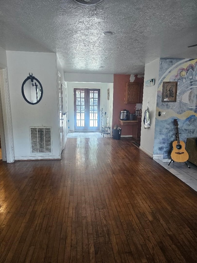 unfurnished living room featuring a textured ceiling, french doors, and dark wood-type flooring