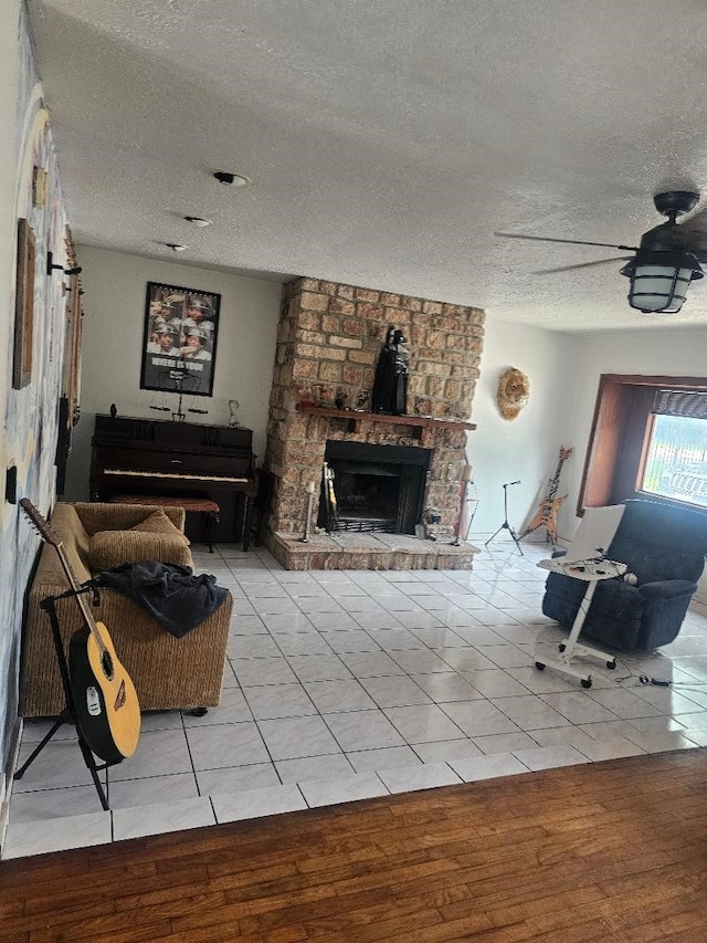 living room featuring wood-type flooring, ceiling fan, a stone fireplace, and a textured ceiling