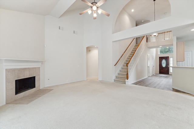 unfurnished living room with carpet flooring, ceiling fan, a towering ceiling, and a fireplace