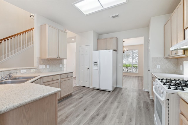 kitchen with a notable chandelier, white appliances, backsplash, and light wood-type flooring