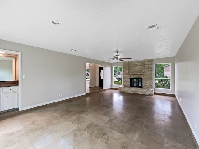 unfurnished living room with tile flooring, ceiling fan, a brick fireplace, and a textured ceiling