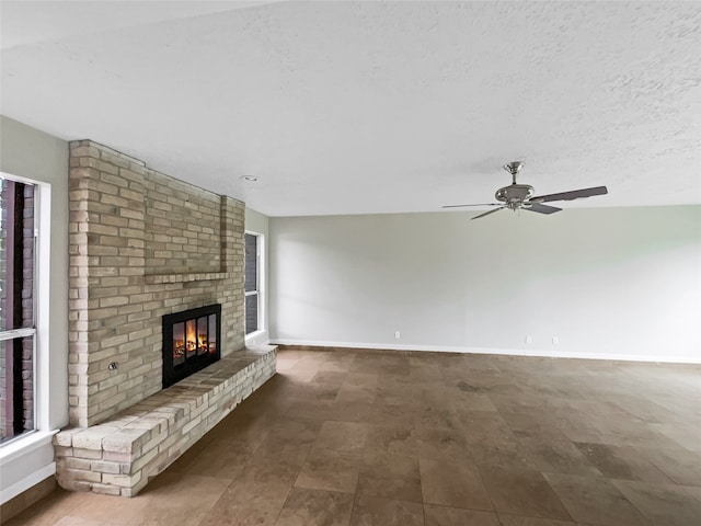 unfurnished living room featuring ceiling fan, a fireplace, a textured ceiling, brick wall, and tile floors