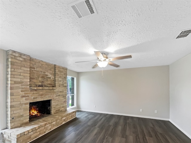 unfurnished living room featuring ceiling fan, brick wall, dark hardwood / wood-style floors, a textured ceiling, and a fireplace