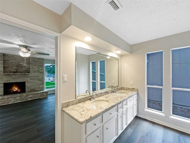 bathroom with a textured ceiling, ceiling fan, hardwood / wood-style flooring, and a stone fireplace