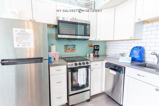 kitchen featuring appliances with stainless steel finishes, light hardwood / wood-style flooring, tasteful backsplash, white cabinetry, and sink