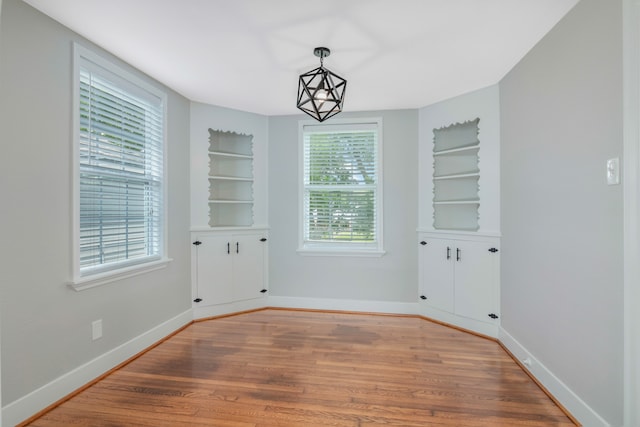 spare room with built in shelves, plenty of natural light, and light hardwood / wood-style flooring