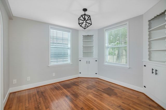 spare room with built in shelves, plenty of natural light, and wood-type flooring