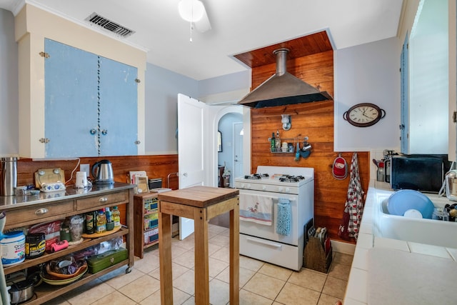 kitchen featuring exhaust hood, ceiling fan, light tile floors, white range with gas stovetop, and wood walls