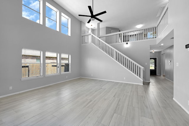 unfurnished living room with light hardwood / wood-style flooring, ceiling fan, and a high ceiling