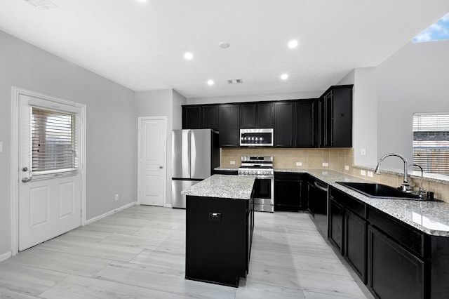 kitchen featuring a center island, light stone countertops, stainless steel appliances, sink, and tasteful backsplash