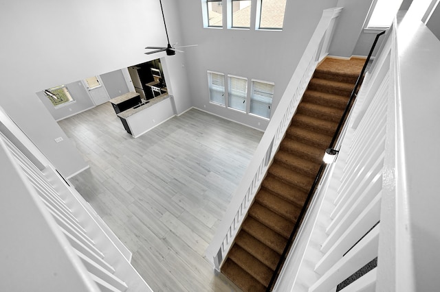 stairway with ceiling fan, light hardwood / wood-style flooring, and a towering ceiling