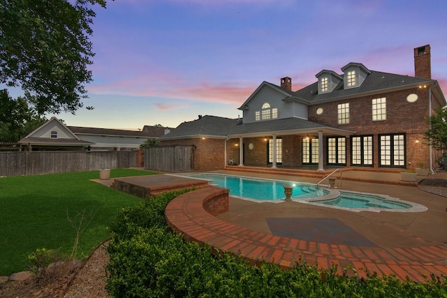 pool at dusk featuring a lawn and a patio area