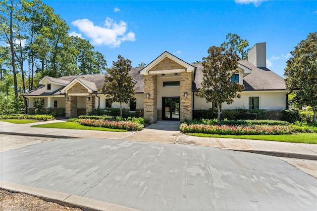 view of front of home with stone siding, a chimney, roof with shingles, and stucco siding