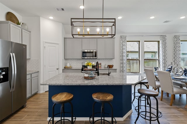 kitchen with a kitchen island with sink, wood finish floors, visible vents, a kitchen breakfast bar, and appliances with stainless steel finishes