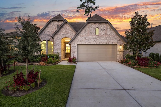 french provincial home with a garage, concrete driveway, brick siding, and a front yard