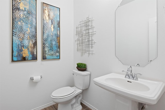 half bathroom with wood finished floors, a sink, toilet, and baseboards