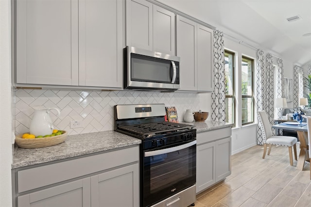 kitchen with appliances with stainless steel finishes, light stone countertops, visible vents, and tasteful backsplash