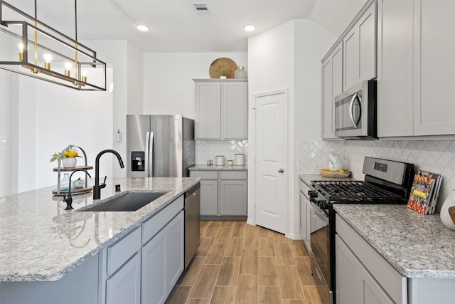 kitchen featuring stainless steel appliances, a sink, visible vents, tasteful backsplash, and an island with sink